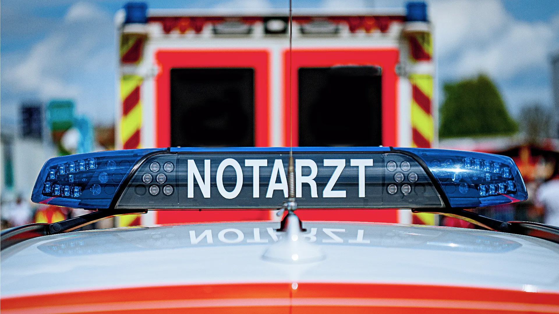 Ein Einsatzfahrzeug mit blauem Blaulicht und der Aufschrift „NOTARZT“ steht vor einem weiteren Rettungsfahrzeug mit roten und gelben Warnmarkierungen.